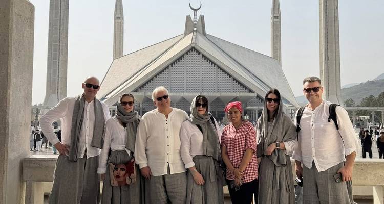 Huit visiteurs prennent la pose devant la saisissante mosquée Faisal avec son toit triangulaire blanc et ses hauts minarets.