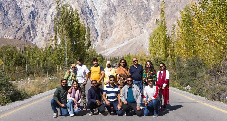 Un grand groupe de touristes s'agenouille et se tient debout sur une route de montagne bordée de peupliers dorés et de falaises rocheuses imposantes.