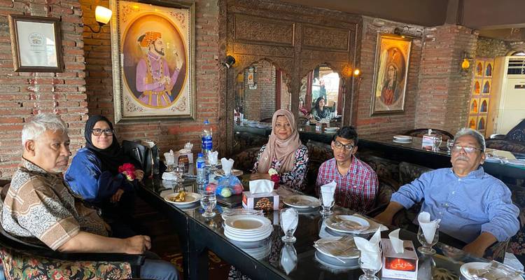 Une famille est assise autour d'une table dressée à l'intérieur d'un restaurant rustique aux murs de briques décoré de peintures traditionnelles.