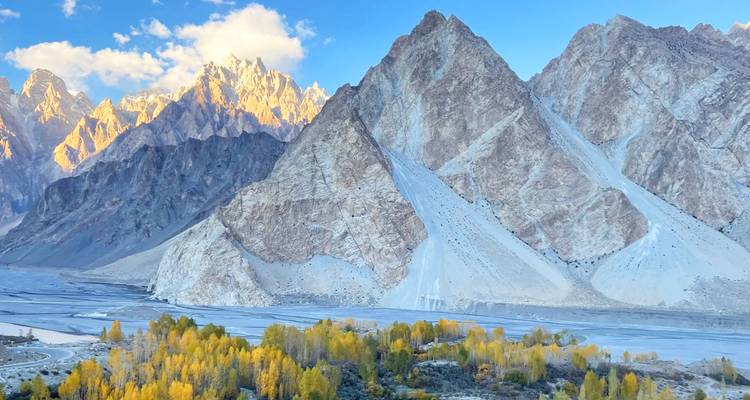 Des pics de granit déchiquetés brillent dans une lumière dorée au-dessus d'une plaine de rivière tressée parsemée d'arbres automnaux jaunes.