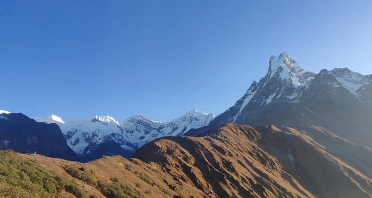 Sharp Machapuchare peak rising above brown ridges and blue sky.