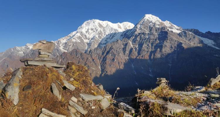 Stone cairns stacked on ridge with bold snow-clad peaks beyond.