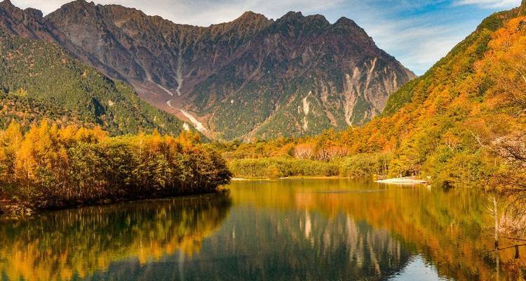 Stille meer dat herfstwouden en hoge ruige bergen weerkaatst.