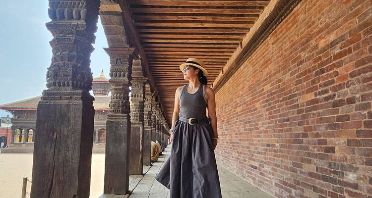 Stilvolle Frau, die entlang einer historischen Holzkolonnade in einem nepalesischen Innenhof geht.