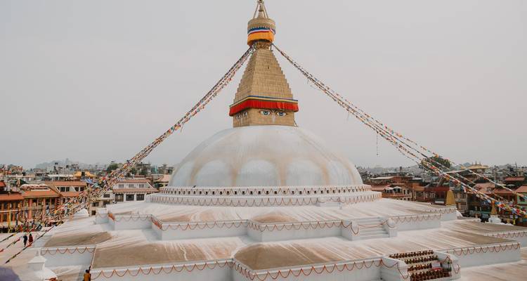 Le dôme blanc colossal et la flèche dorée du stupa de Boudhanath drapés de drapeaux de prière s'élèvent au-dessus des toits de Katmandou.