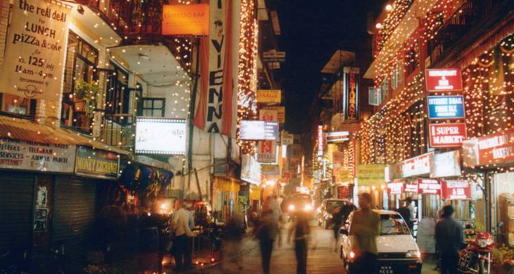 Une rue nocturne animée de Thamel brille de panneaux néon colorés et de guirlandes de lumières festives tandis que des piétons flous passent.