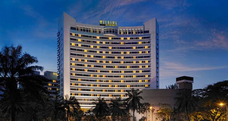 Das Furama RiverFront Hotel beleuchtet in der Abenddämmerung inmitten von Palmen in Singapur.