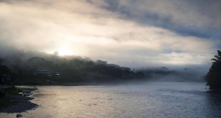 Misty dawn light over a wide jungle river as fog drifts above the water.