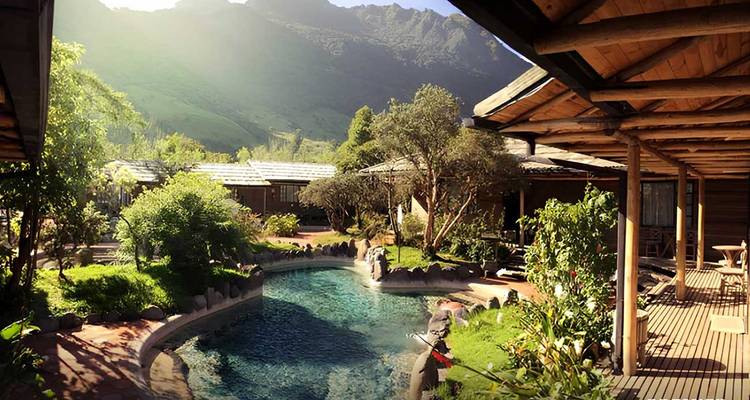Secluded thermal pool surrounded by lush gardens and mountain scenery at a lodge.