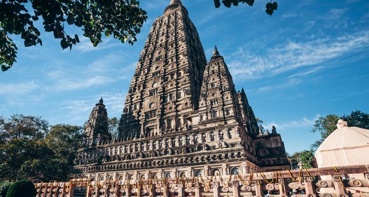 La tour du temple Mahabodhi, richement sculptée, s'élève contre un ciel bleu éclatant, entourée de drapeaux de prière.