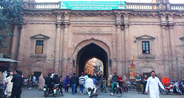 Porte d'entrée animée d'une vieille ville avec des foules, des motos et des boutiques bordant l'arche historique en brique
