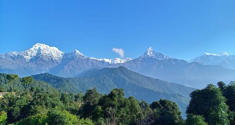 Los picos nevados prístinos del macizo de Annapurna se elevan sobre colinas boscosas bajo un cielo azul sin nubes.