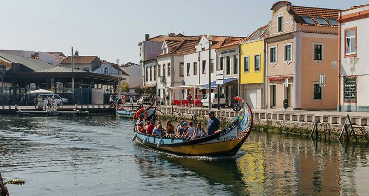 Tourists cruising Aveiro’s canal in a traditional moliceiro boat past pastel waterfront buildings.