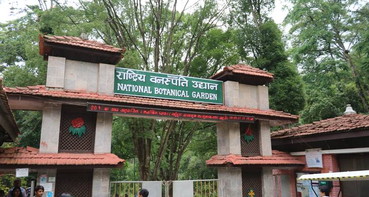Portail en pierre avec un panneau népalais indiquant Jardin botanique national encadré par de grands arbres.