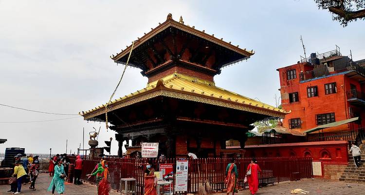 Templo escalonado de techo dorado rodeado de visitantes y barandillas rojas en la cima de una colina