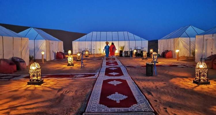 Luxuriöses Wüstencamp bei Nacht, beleuchtet von Laternen und Teppichen unter einem tiefblauen Himmel.