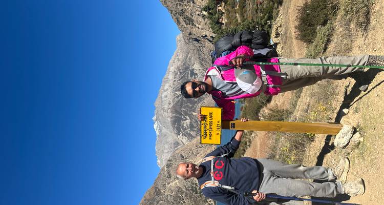 Twee wandelaars die bij een geel bord staan dat de afstand naar het Phoksundo-meer aangeeft met bergen op de achtergrond.