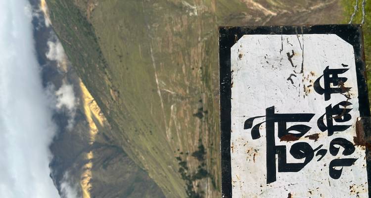 Verweerde bord in Nepalees schrift met terrasvormige groene bergen en wolken op de achtergrond.