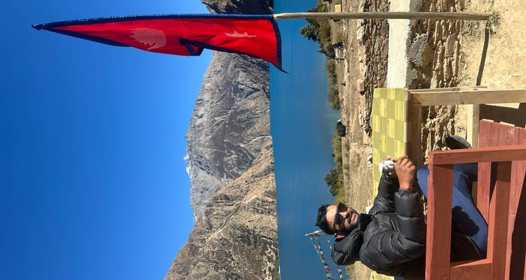 Reiziger geniet van thee op een buitenbank naast het Phoksundumeer met een wapperende Nepalese vlag.