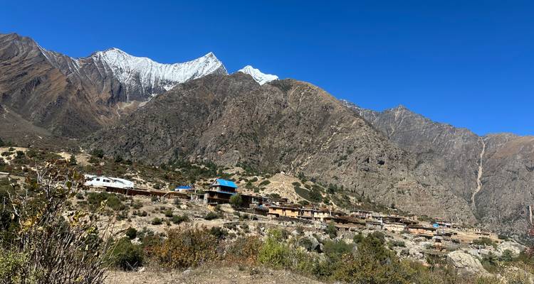 Afgelegen Himalaya-dorp verspreid langs een helling onder grillige met sneeuw bestoven pieken en blauwe lucht.