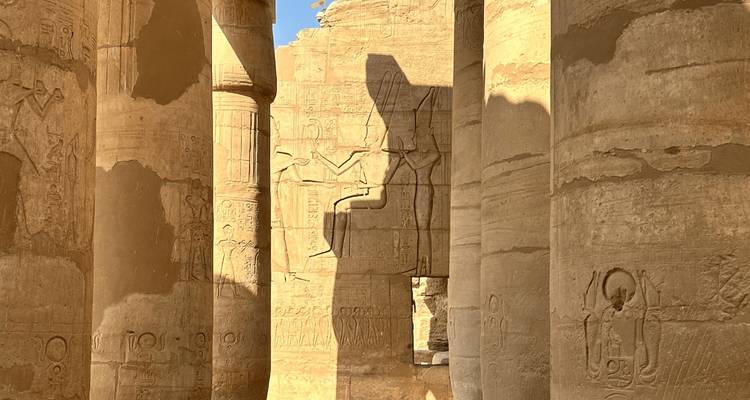 La luz del sol proyecta sombras nítidas a través de imponentes columnas cubiertas de jeroglíficos dentro de un antiguo templo egipcio.