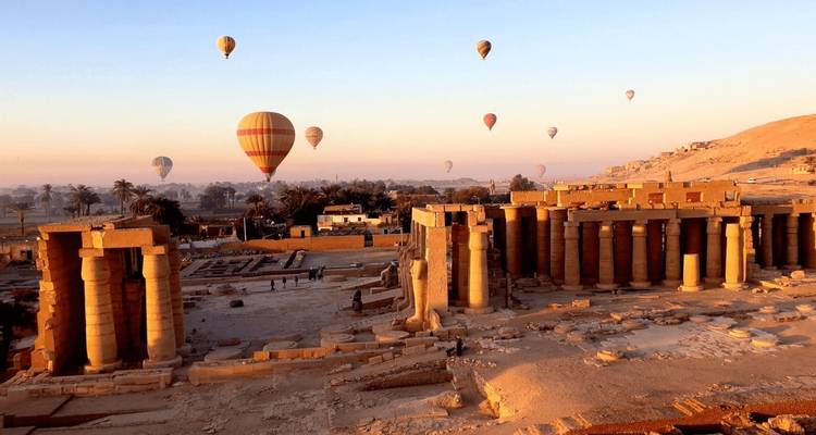 Coloridos globos aerostáticos flotan sobre ruinas monumentales de templos y el valle del Nilo bajo la cálida luz del amanecer.