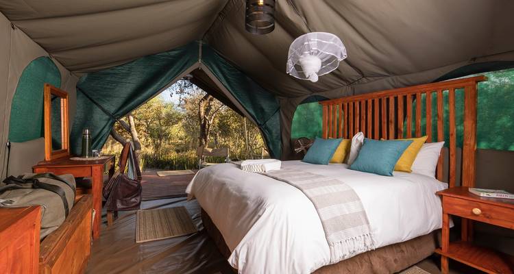 A luxury canvas tent features a plush bed, colourful cushions and views of bushland through the open flap.
