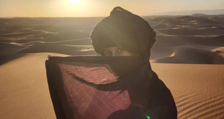 Portrait d'une femme en tenue du désert couvrant partiellement son visage avec un foulard au lever du soleil.