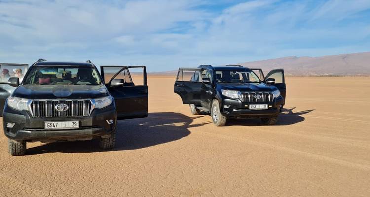 Deux 4x4 noirs garés sur une immense plaine désertique aride sous un ciel bleu éclatant.