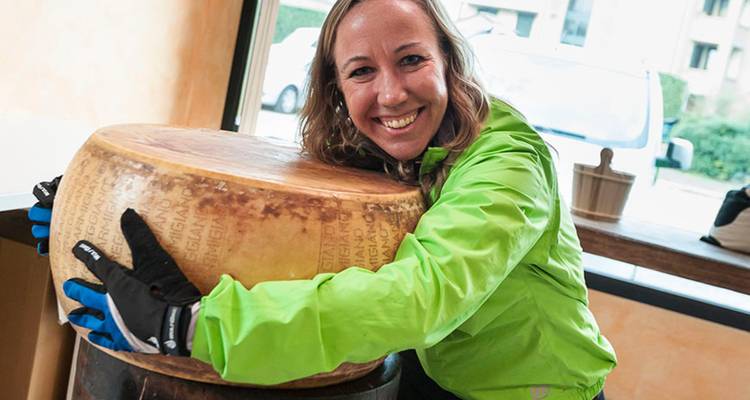 Un passionné souriant embrasse une énorme meule de Parmigiano-Reggiano dans une salle de dégustation.