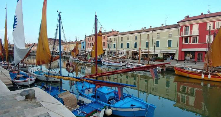 Des voiliers traditionnels colorés bordent un canal paisible entouré de bâtiments aux couleurs pastel dans une ville côtière.