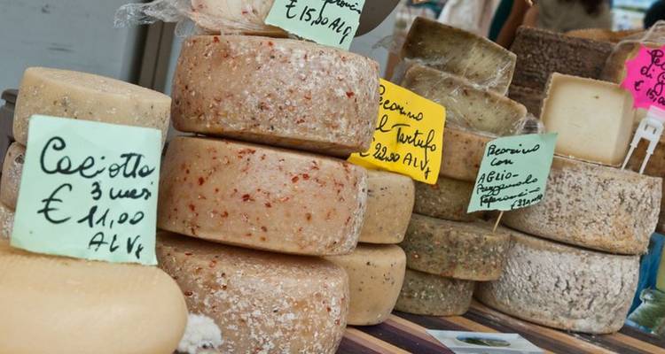 Des piles de fromages fermiers assortis avec des étiquettes de prix manuscrites sont disposées sur une table de marché en bois.