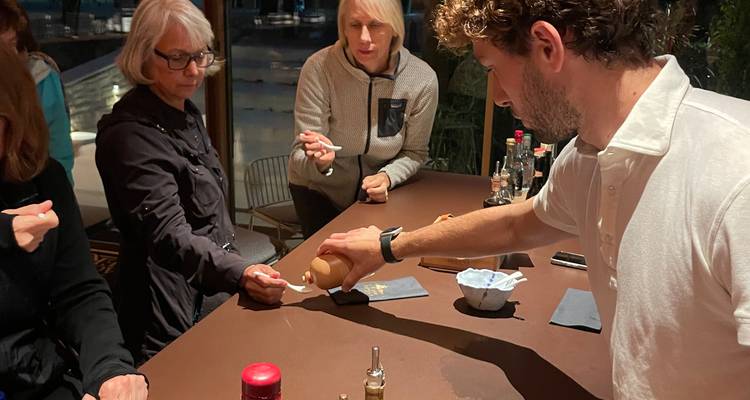 Les invités goûtent une sauce versée par un hôte lors d'une démonstration culinaire intimiste au comptoir.
