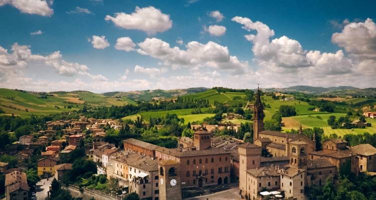 Une vue aérienne d'une pittoresque ville italienne perchée sur une colline, entourée d'une campagne luxuriante en patchwork sous des nuages épars.