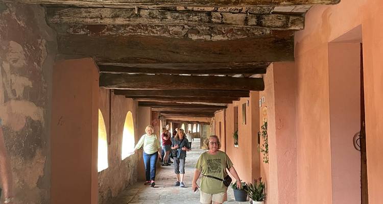 Les visiteurs se promènent dans un corridor couvert rustique avec des poutres en bois patiné et des murs pêche.