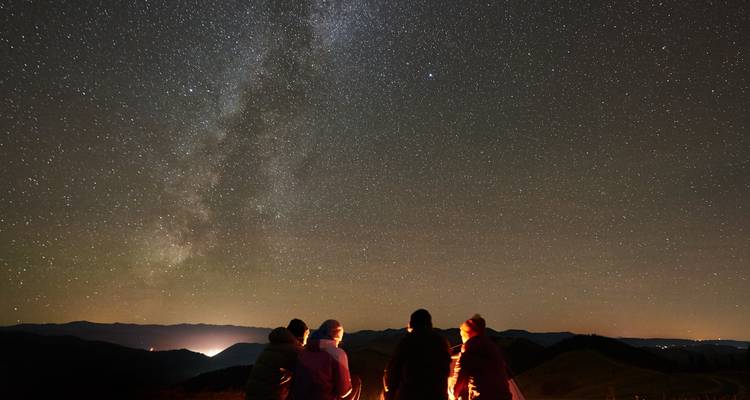 Les campeurs sont assis autour d'un feu chaleureux sous un vaste ciel nocturne rempli de la Voie lactée et d'innombrables étoiles.