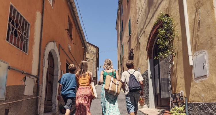 Eine Familiengruppe spaziert an einem sonnigen Tag eine schmale Gasse zwischen rustikalen italienischen Gebäuden hinauf