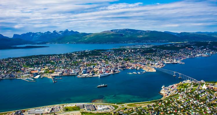 Farbenfrohe Luftaufnahme der Stadt Tromsø, des Fjords, der Brücke und der umliegenden Berge unter blauem Himmel