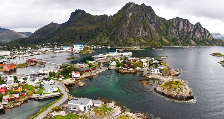 Luftaufnahme des Dorfes Reine mit dramatischer Bergkulisse und türkisfarbenen Buchten