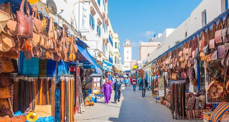Calle colorida del zoco bordeada de artículos de cuero y textiles bajo el cielo azul brillante de Marruecos.