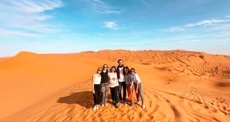 Grupo de amigos posando en la cima de dunas naranjas del Sahara bajo un cielo azul despejado.