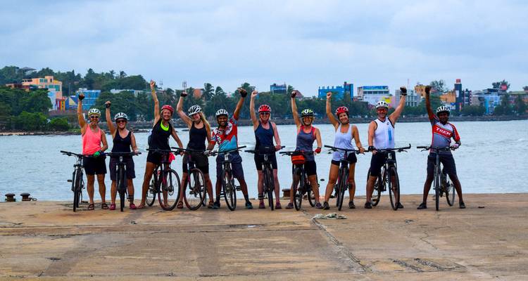 Des cyclistes casqués se tiennent debout, le poing levé, sur une jetée en béton au bord d'eaux côtières calmes et d'un horizon coloré.