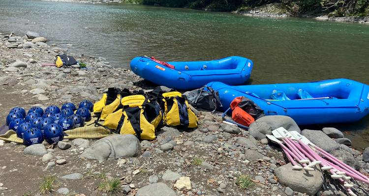 Inflatable blue rafts, helmets and dry bags laid out on a rocky riverbank ready for white-water rafting.