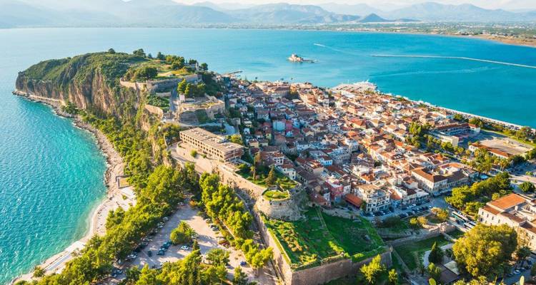 Sun-bright aerial of Nafplion peninsula with emerald waters and sprawling old town, mirrored cliffs to the left.