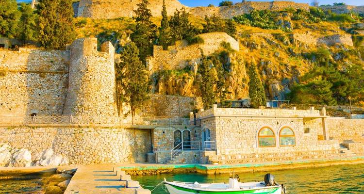 Golden evening light on Nafplion’s fortress walls reflected in the harbor beside a small white boat.