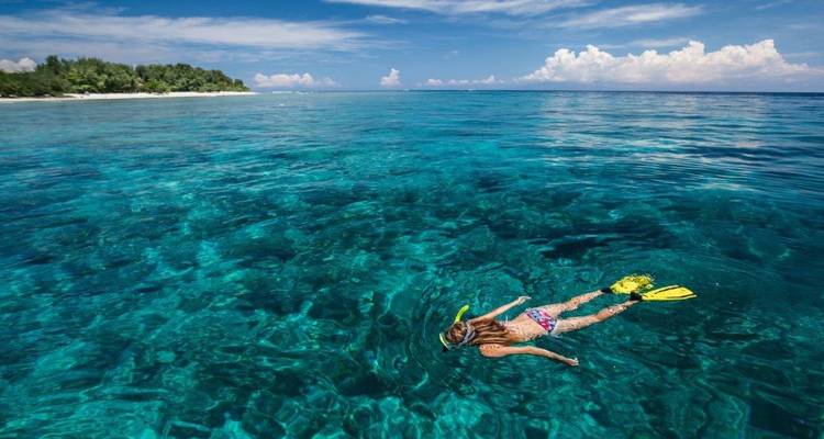 Snorkelaar drijvend boven kristalheldere koraalrif in helderblauwe tropische wateren.