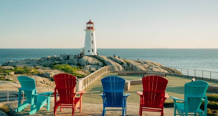 Des chaises Adirondack colorées font face au phare emblématique de Peggy's Cove, perché sur une pointe rocheuse à l'heure dorée.