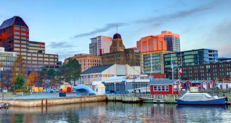 Des bâtiments colorés et des bateaux bordent le front de mer dynamique d'Halifax sous un ciel de lever de soleil doux.