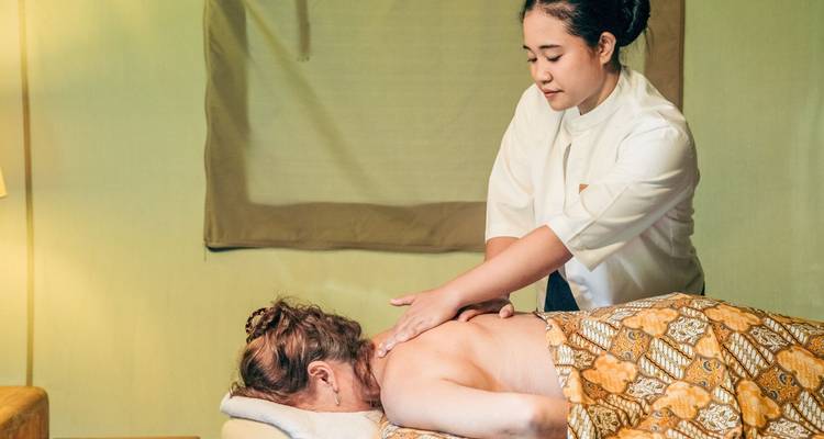Spa therapeut die een ontspannende rugmassage geeft in een tentenkamer.