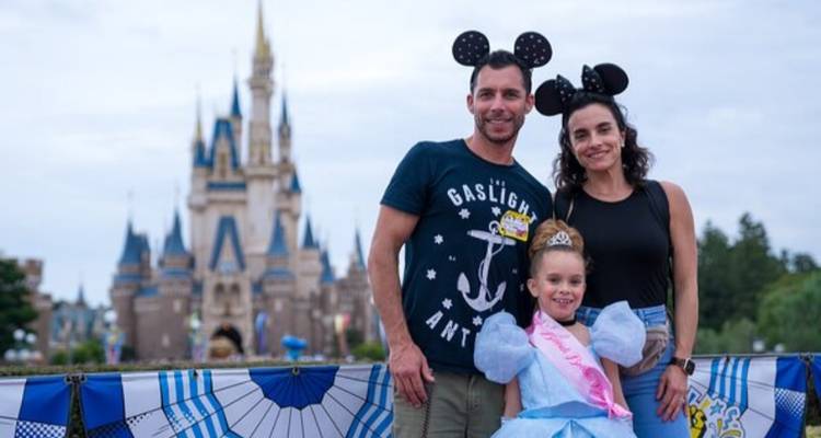Glimlachende familie met Mickey Mouse-oren die poseert voor een sprookjeskasteel in een pretpark.